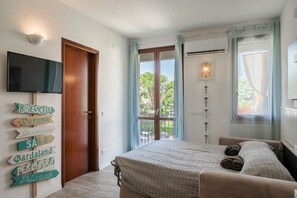 A hotel room with a bed, a TV, a window with curtains, and wall decorations with place names.
