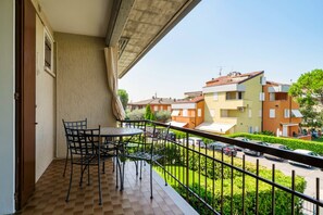 A balcony with a table and chairs, overlooking a parking area and neighboring buildings.