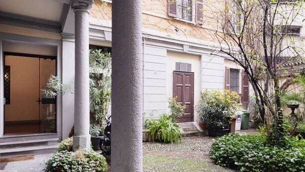Un patio con un edificio que tiene una puerta marrón, plantas en macetas y un camino de piedra.