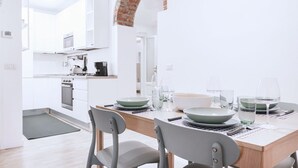 Una cocina moderna con armarios blancos, un arco de ladrillo y un comedor con una mesa de madera dispuesta para cuatro.