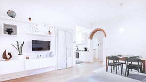Una sala de estar moderna con un televisor de pantalla plana, muebles blancos y un comedor con un arco de ladrillo.