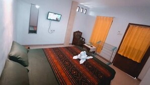 A bedroom with a bed, a television, a mirror, and a window with curtains. - Hotel O Balekui Homestay (Pujut)