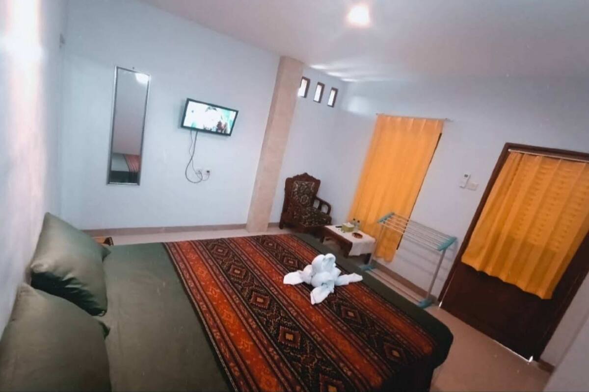 Un dormitorio con cama, televisión, espejo y ventana con cortinas.