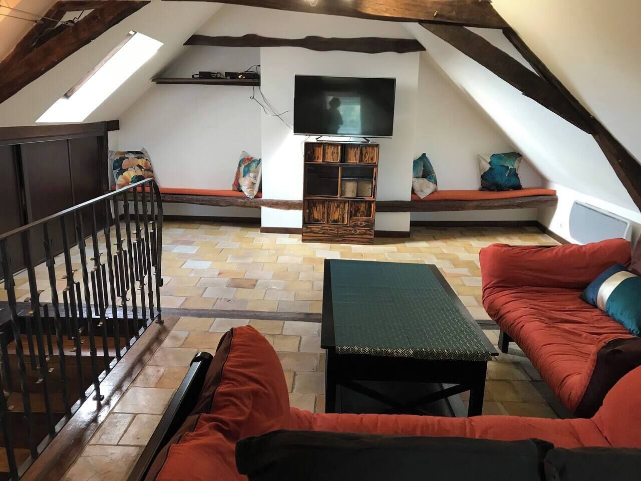 Quarto no sótão com cama beliche, sofá, mesa pequena e televisão fixada na parede.