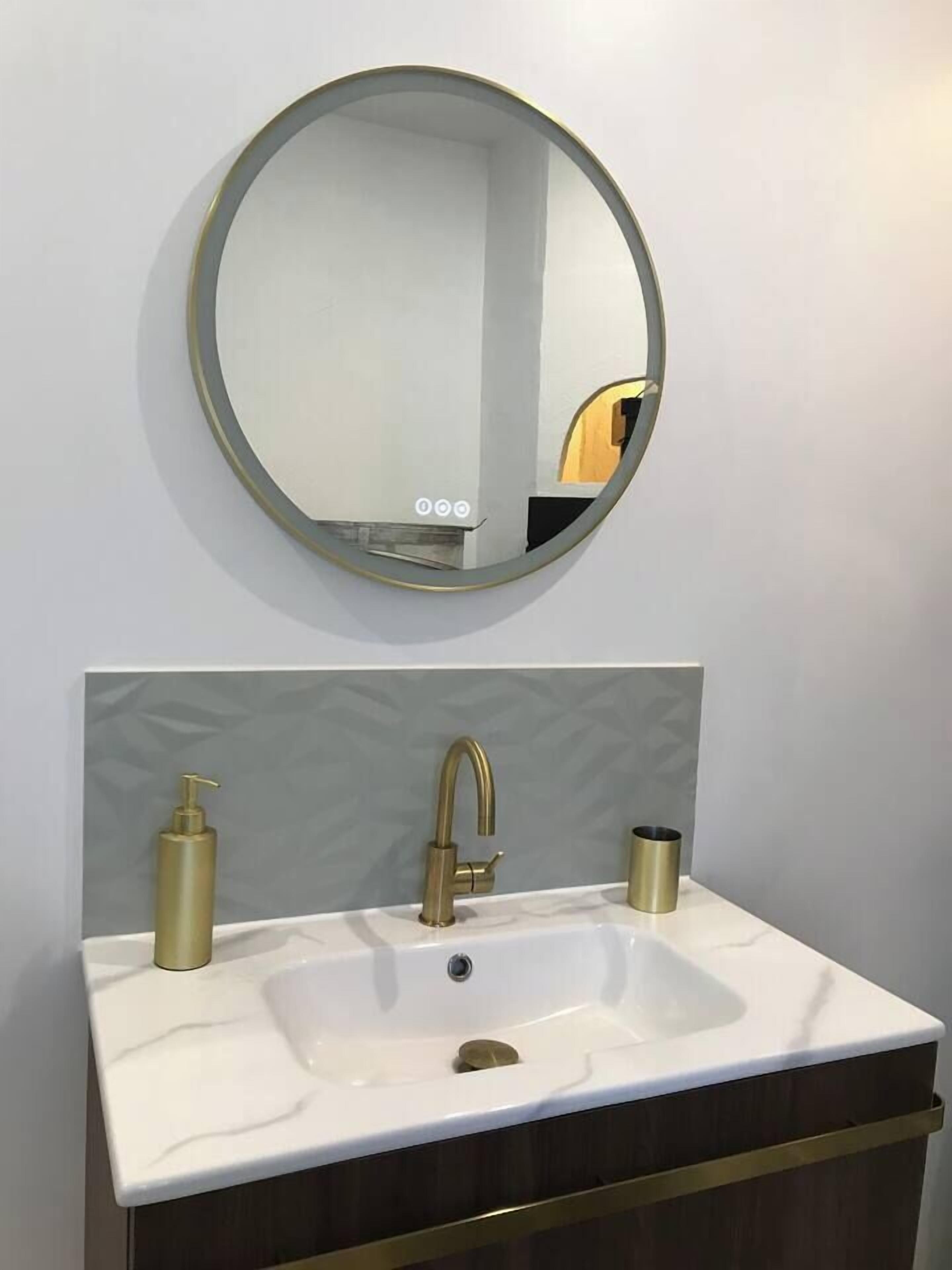 A bathroom with a white sink, gold faucets, and a round mirror.