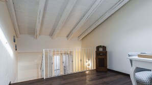 A spacious room with a high ceiling and wooden beams, a white railing, and a wooden cabinet. - Casa Florus by Wonderful Italy (Syracuse)