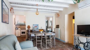A living room with a sofa, a dining table with chairs, a TV on a stand, and a kitchen in the background. - Casa Florus by Wonderful Italy (Syracuse)