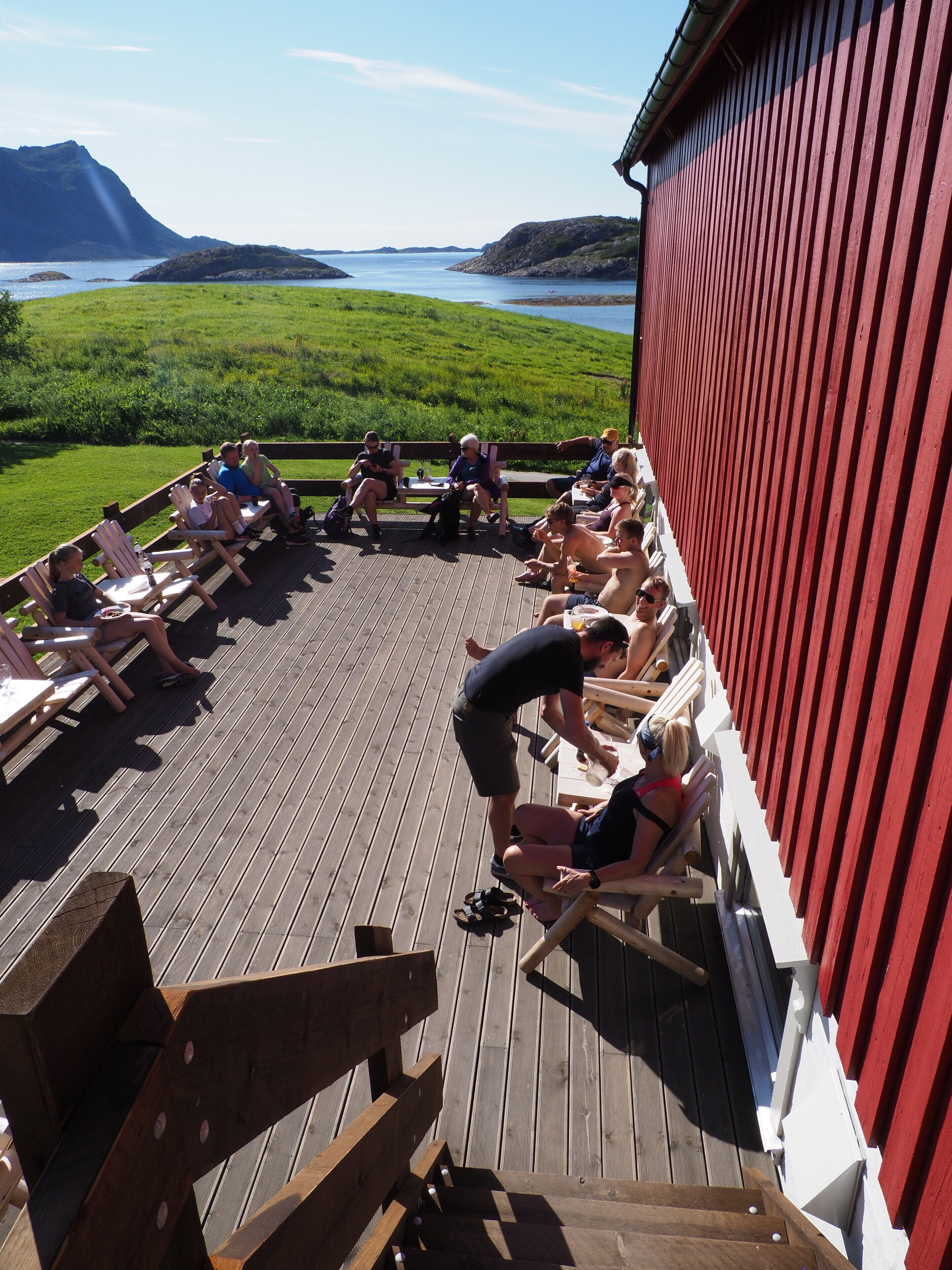 A group of people seated on deck chairs on a wooden deck with a view of a green landscape and water.