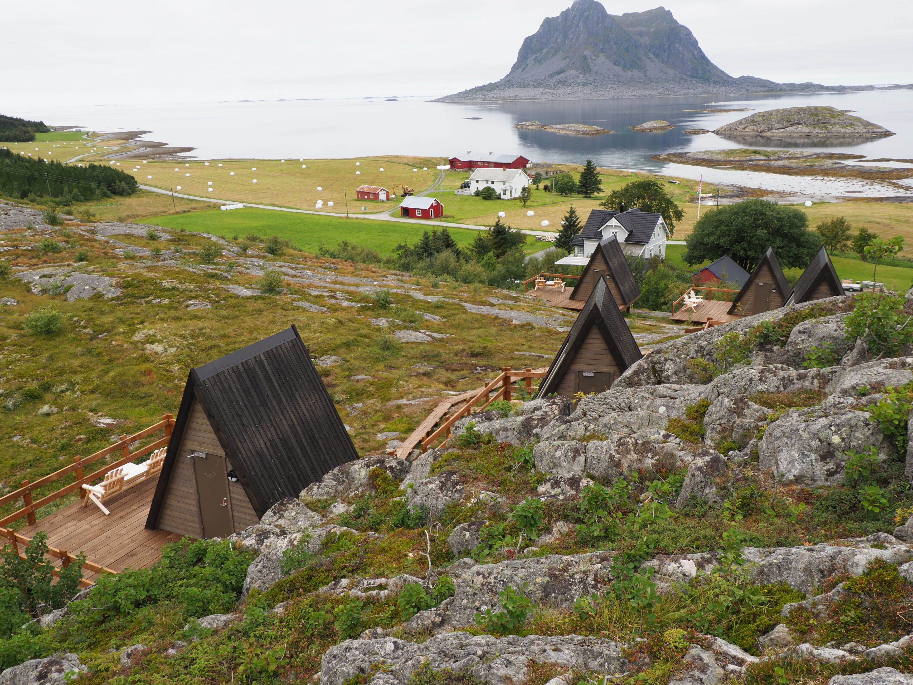 A mountainous area with several wooden cabins and a large house with a red roof.