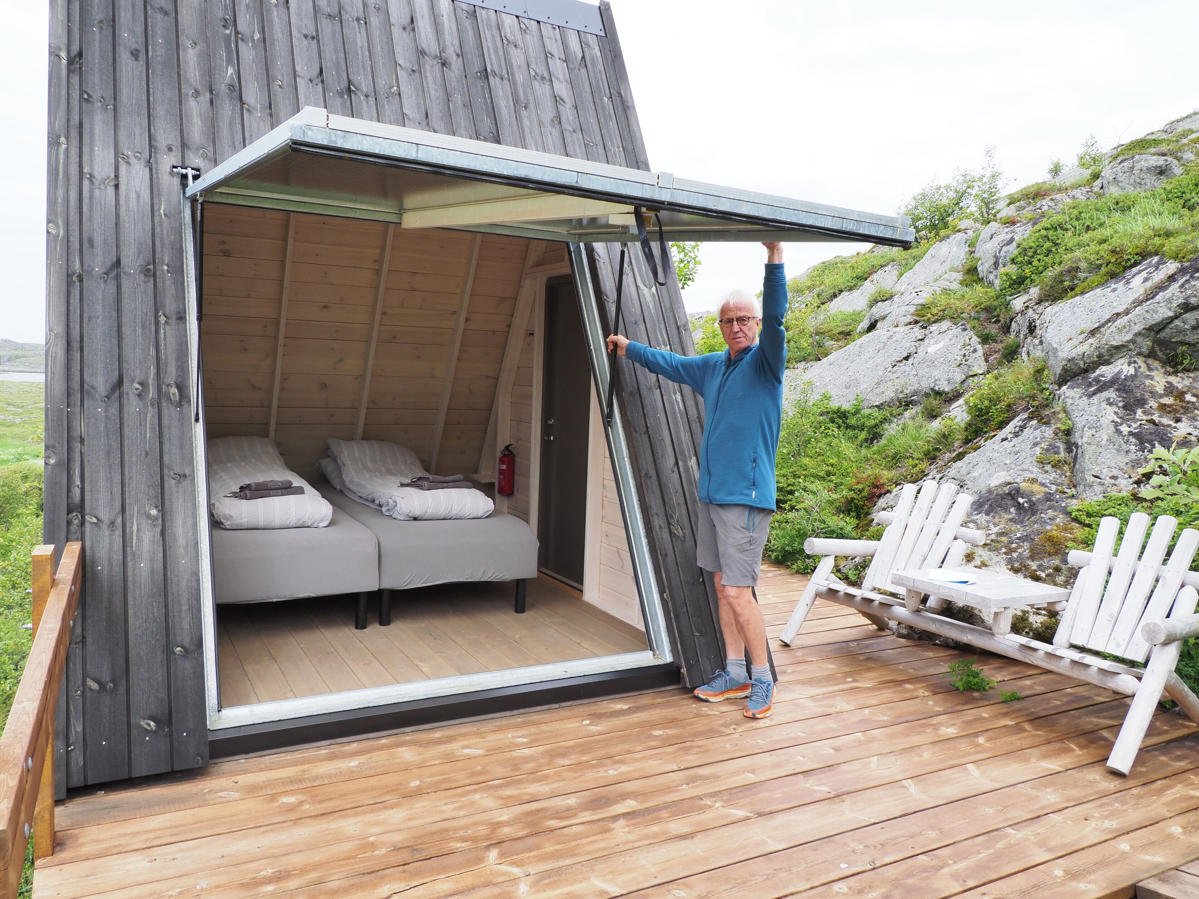 A wooden cabin with a bed inside, a fire extinguisher on the wall, and a person opening the door.