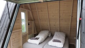 Une petite pièce chaleureuse, avec deux lits, une fenêtre et des murs en bois.