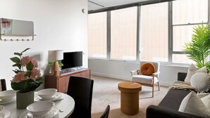 Un salon moderne avec un coin repas, de grandes fenêtres et un téléviseur.