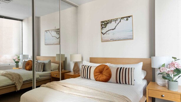 Une chambre d’hôtel moderne, dotée d’un grand lit, d’une table de chevet, d’un miroir et de deux lampes fixées au mur.