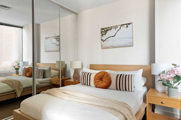 A modern hotel room with a large bed, a nightstand, a mirror, and two wall-mounted lamps.