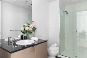 A modern bathroom with a white sink, a glass shower enclosure, and a vase of pink flowers on the vanity.