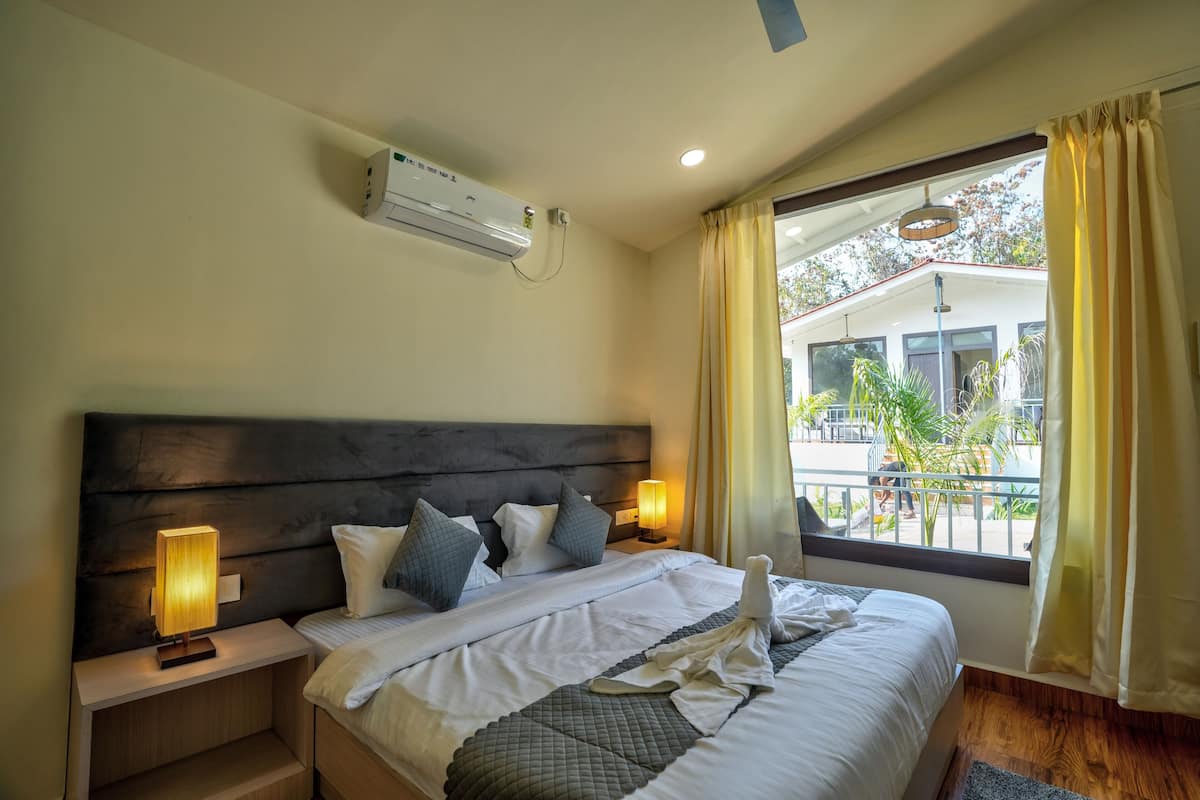 A hotel room with a large bed, bedside lamps, an air conditioning unit, and a view of the outside.