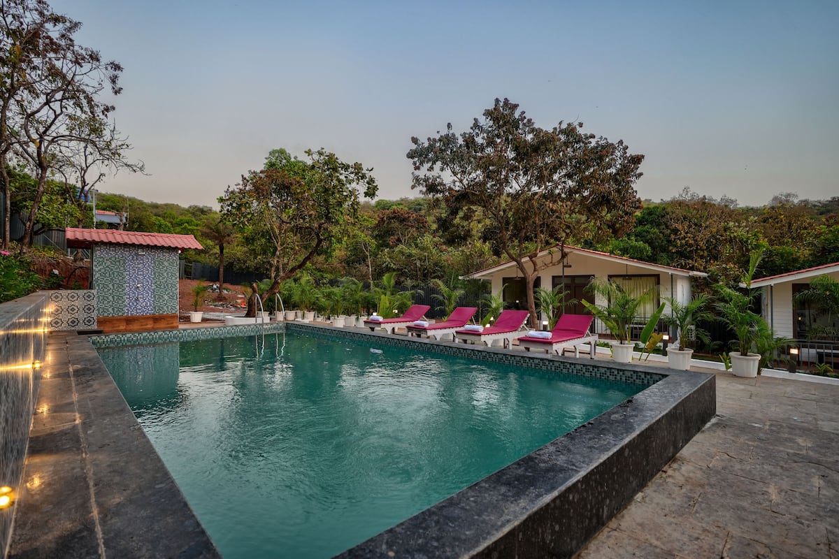 A swimming pool with a tiled edge, surrounded by lounge chairs and potted plants.