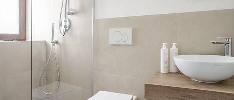 A modern bathroom with a glass-enclosed shower, a white toilet, and a wooden vanity with a large white sink.
