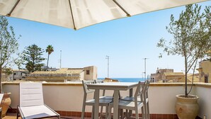 A terrace with a table and chairs, overlooking a coastal view with buildings and trees. - La terrazza sul vicolo della Giudecca by Wonderful Italy (Syracuse)