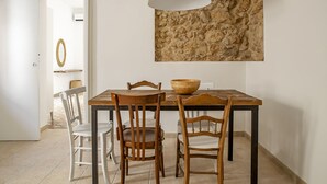 A dining area with a wooden table and chairs, a stone accent wall, and a pendant light. - La terrazza sul vicolo della Giudecca by Wonderful Italy (Syracuse)