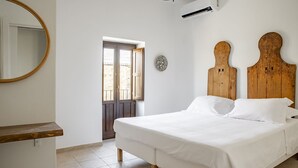 A bedroom with a wooden headboard, a bed with white linens, a round mirror, and a door leading outside. - La terrazza sul vicolo della Giudecca by Wonderful Italy (Syracuse)