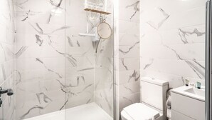 Une salle de bain carrelée de marbre, dotée d’une douche en verre, de toilettes et d’un lavabo avec un flacon de la marque LUX.