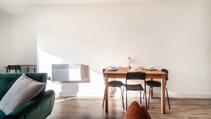 Un salon moderne avec un canapé vert, une table à manger dressée pour quatre personnes et un grand appareil de climatisation fixé au mur.