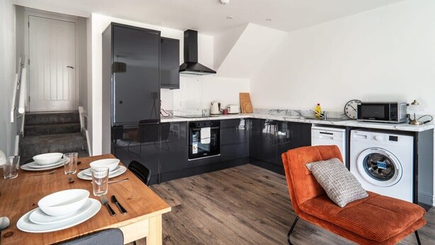 Une cuisine moderne avec des meubles de couleur noire, un four encastré, un four à micro-ondes et un lave-linge.