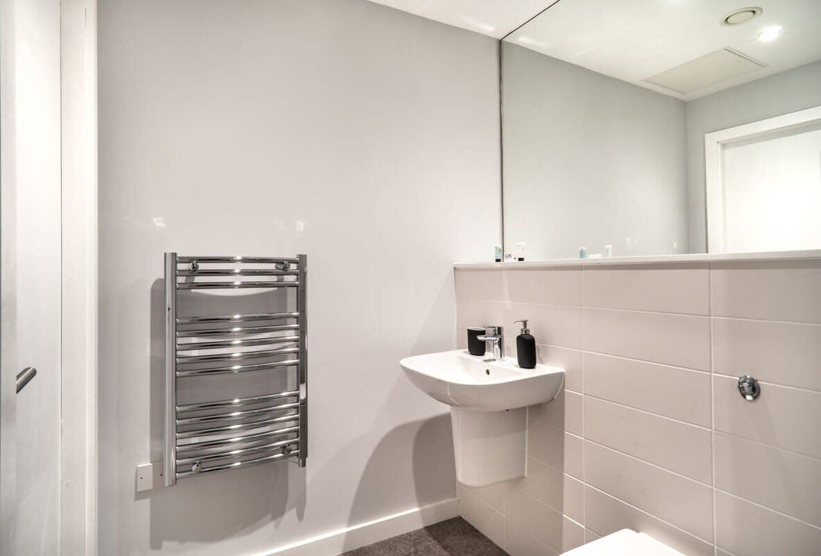 Une salle de bain moderne avec un lavabo blanc, un porte-serviettes chromé et un grand miroir.