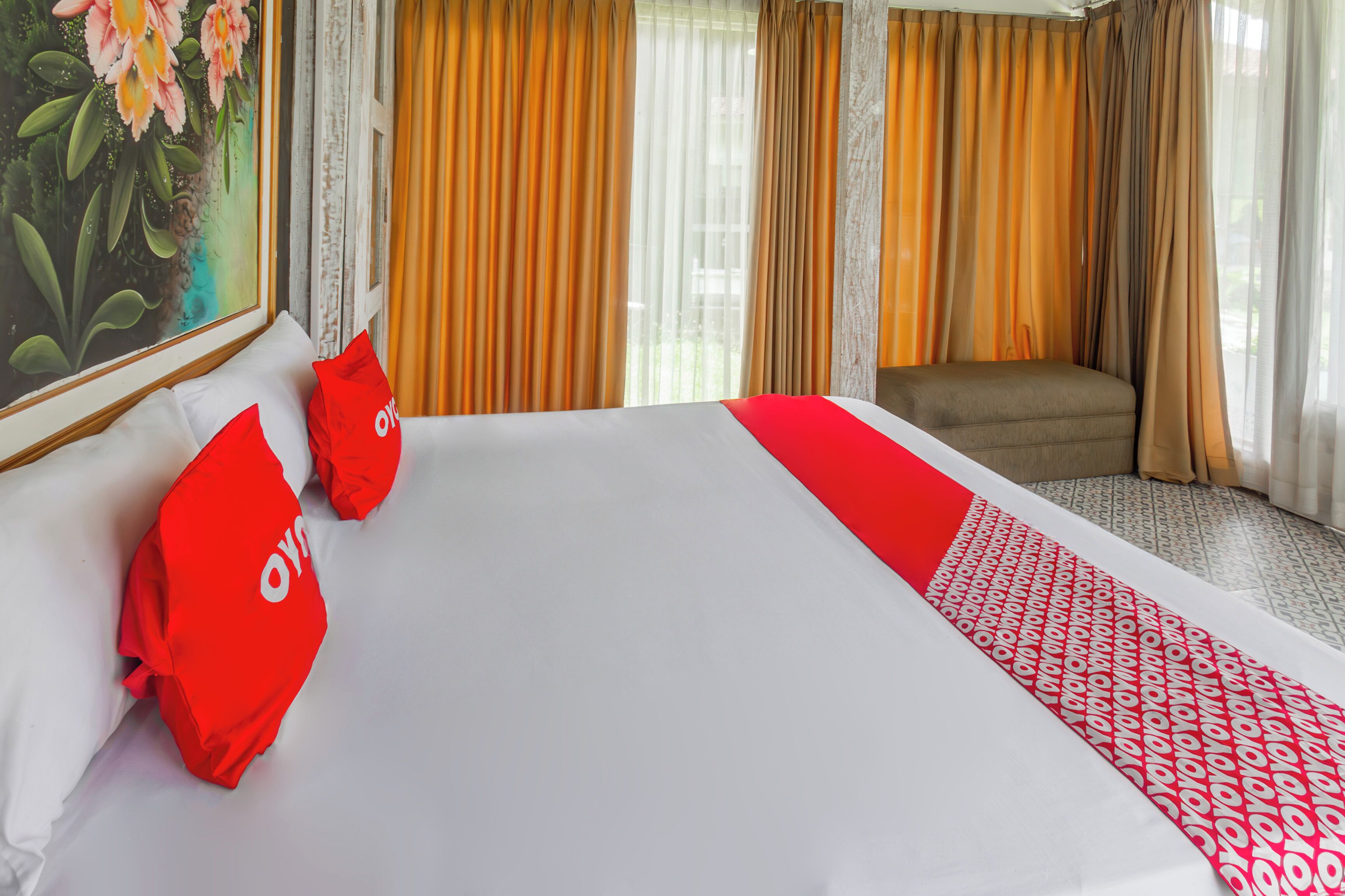 Una habitación de hotel con una cama grande, almohadas rojas, un plaid estampado y cortinas.