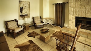 Un salon avec une cheminée en pierre, deux fauteuils en bois, une petite table et un tapis en fourrure.
