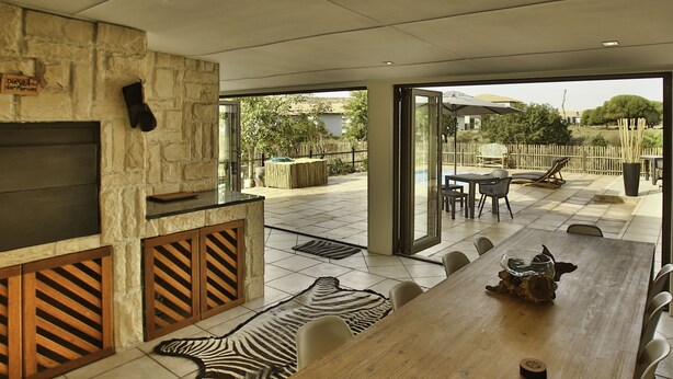 Une vaste terrasse dotée d’une table à manger en bois, de chaises et d’un tapis à motifs zébrés.