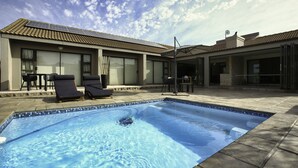 Une piscine avec des chaises longues, un patio couvert et un bâtiment doté d’un toit en tuiles.