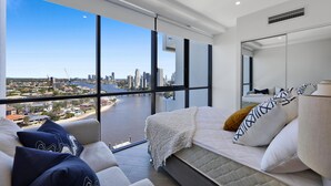 A modern bedroom with a city view, a large bed, and a sofa.