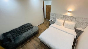 Un dormitorio con una cama, un sofá gris, suelo de madera y cabecera de mármol.