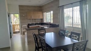 A modern kitchen with a central island, dining table with chairs, and large windows with curtains. - Impeccable 3-bed Villa in Anse Boileau! (Mahé Island)