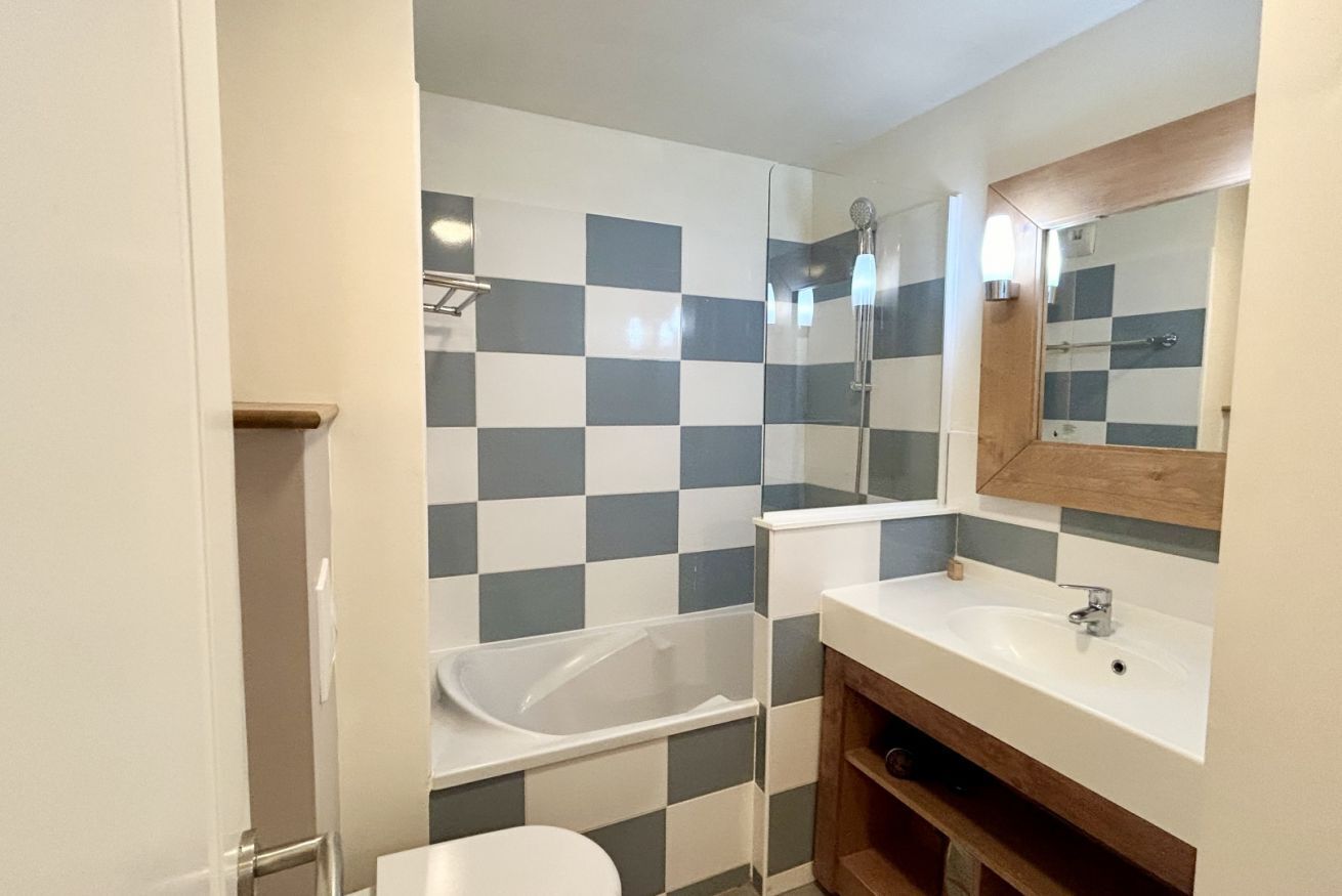 Une salle de bain avec un mur recouvert de carreaux à motifs géométriques, une baignoire, un lavabo et un miroir.
