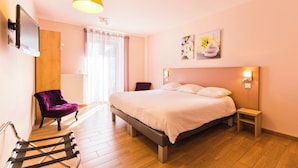 Un dormitorio con una cama, una silla, una mesita, un televisor y una ventana con cortinas.