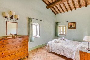 A bedroom with a wooden dresser, a bed with a white bedspread, a window with curtains, and a wooden ceiling. - Apartment for family (colle di val d'elsa)