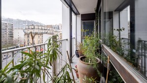Un balcon agrémenté de plantes en pot, avec vue sur des immeubles et une rambarde en métal.