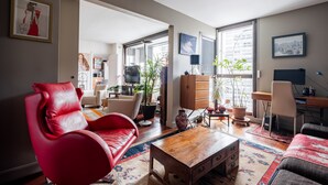 Un salon moderne avec un canapé en cuir rouge, une table basse en bois et une vue sur la ville grâce à de grandes fenêtres.