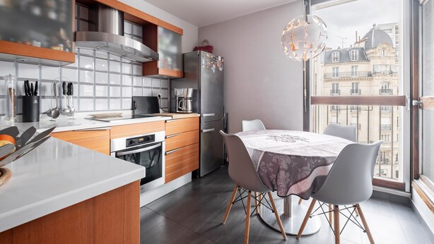 Une cuisine moderne avec un coin repas, de grandes fenêtres et une vue sur les immebles.