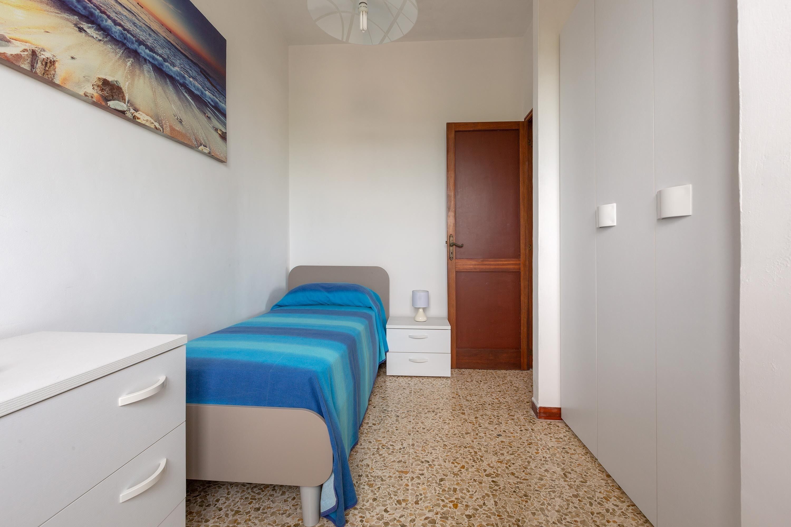 A bedroom with a bed, a nightstand, a dresser, and a door.