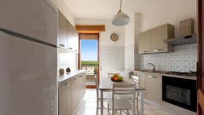 A kitchen with a view, white cabinets, a stove, and a dining table with chairs. - 3730 Appartamento Valencia by Barbarhouse (Porto Cesareo)