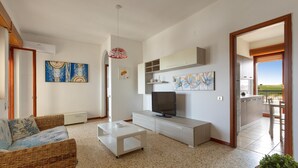 A modern living room with a television, sofa, and coffee table. There are paintings on the walls and a view of the outdoors through an open door. - 3730 Appartamento Valencia by Barbarhouse (Porto Cesareo)