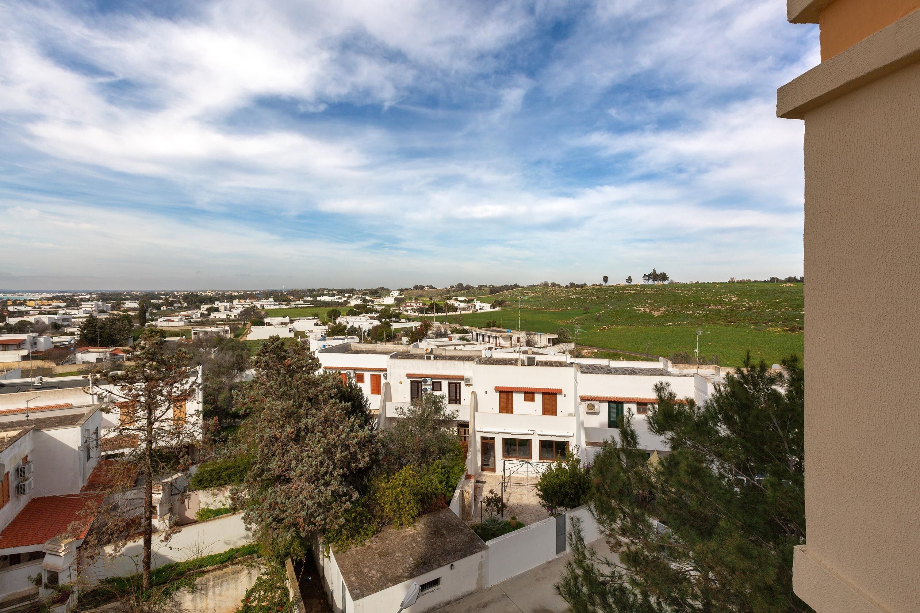 A residential area with white buildings, green spaces, and a clear sky.