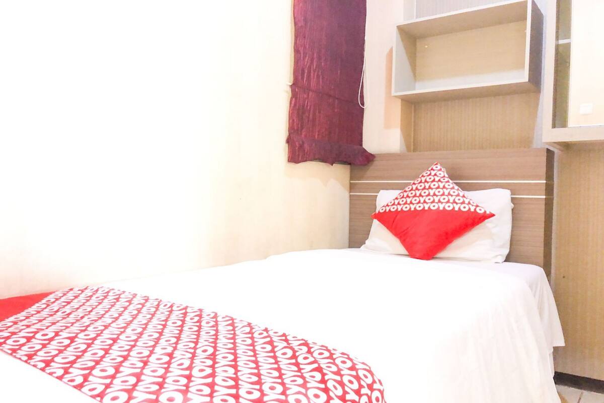 Una cama con una colcha estampada en blanco y rojo, un cojín rojo y blanco y un cabecero de madera.