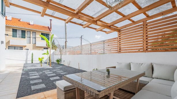 A covered patio with a table and sofa, a tiled floor, and a view of a building with a tiled roof. - Cozy Retreat - By Wehost (Funchal)