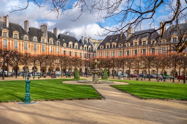 A courtyard with a fountain, surrounded by a park with neatly trimmed grass and trees.