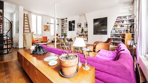 Ein geräumiges Wohnzimmer mit einem Holztisch, einem violetten Sofa und einem Bücherregal voller Bücher.